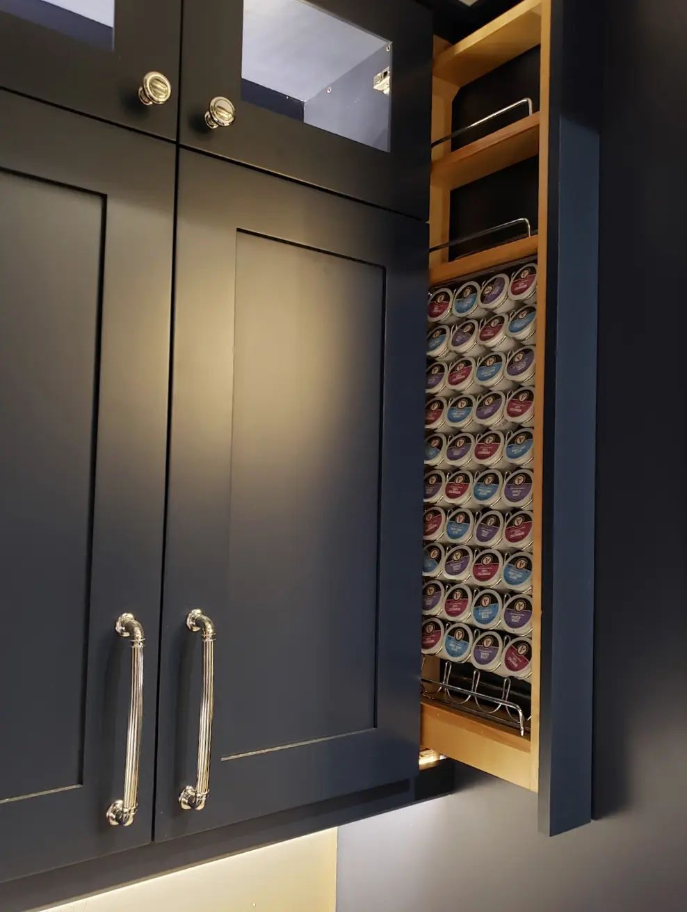 Black kitchen cabinets with chrome handles beside a pull-out spice rack filled with jars.
