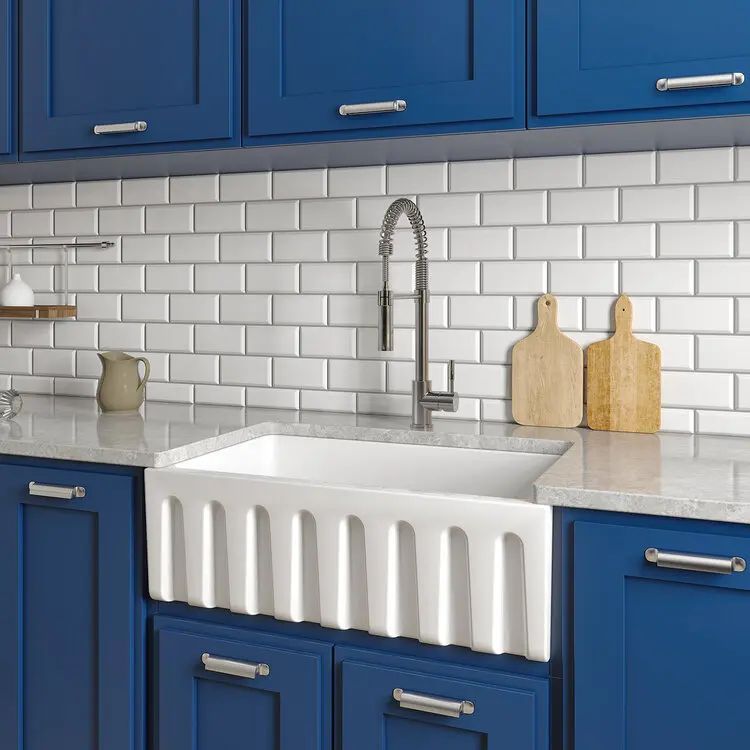 Blue kitchen with white tile backsplash, marble counter, farmhouse sink, and chrome faucet
