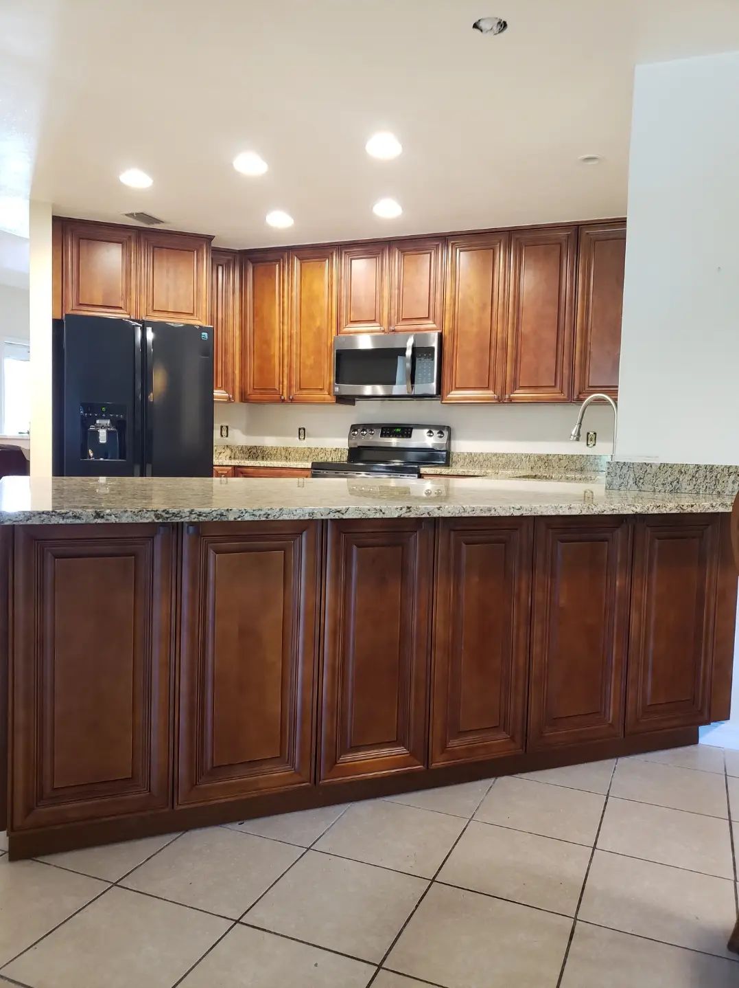 Modern kitchen with wood cabinets, granite countertops, black appliances, and tiled floor.