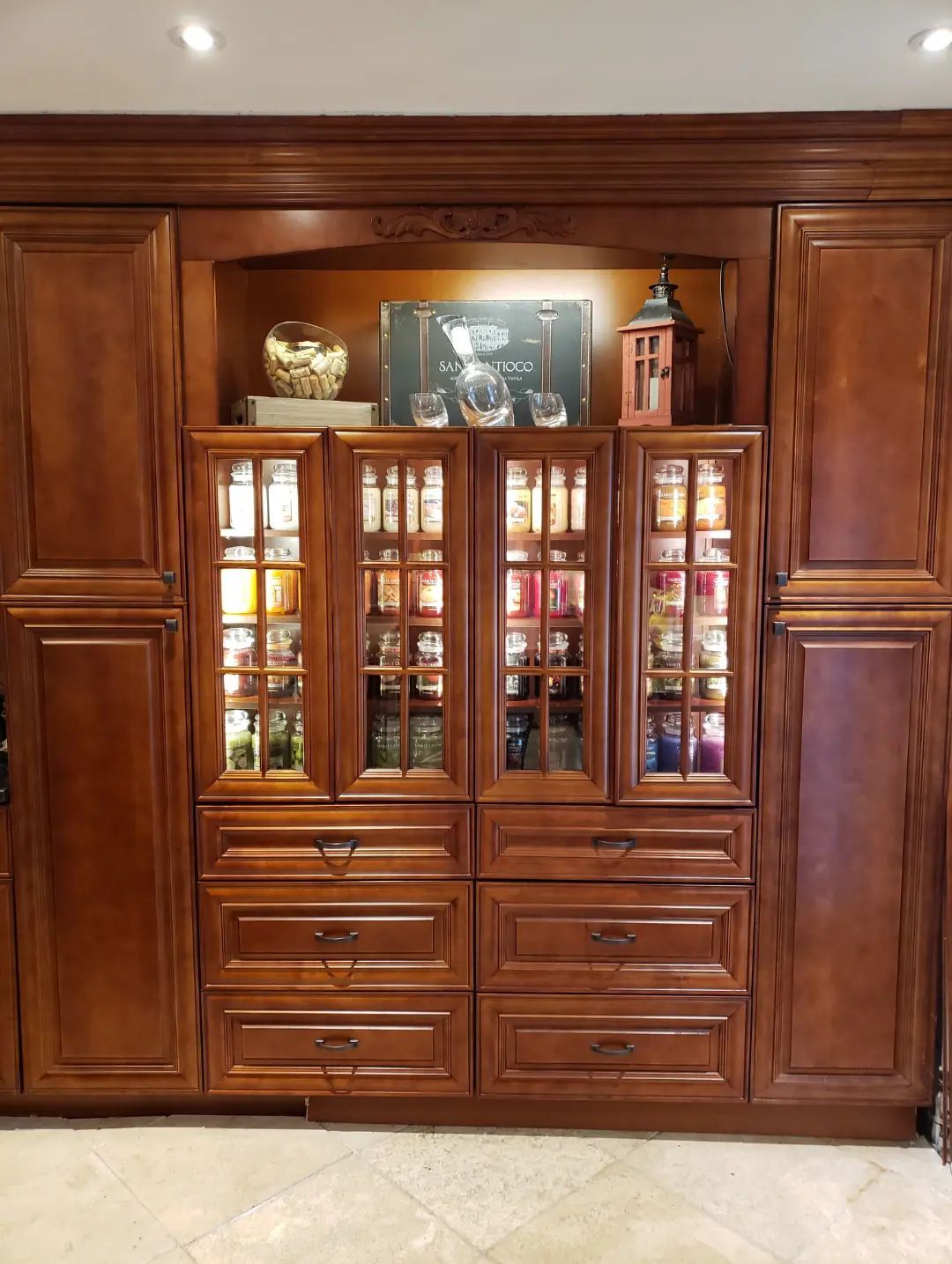 Wooden built-in cabinet with glass display doors and drawers, filled with dishes and decorative items.