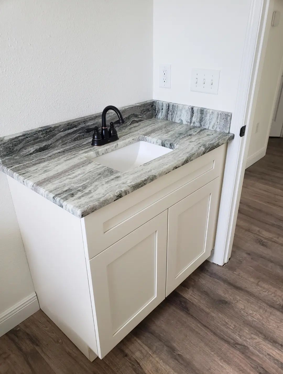 Small bathroom vanity with granite countertop, black faucet, and wood-look flooring