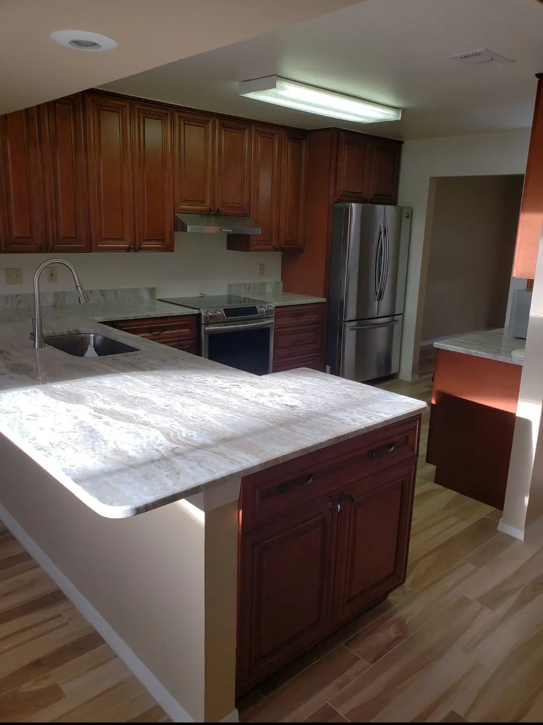 Modern kitchen with wood cabinets, white countertops, stainless steel fridge, and island under fluorescent lights