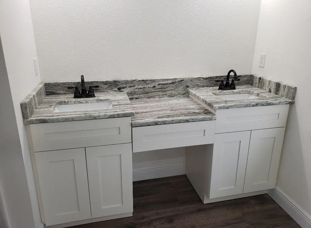 Bathroom vanity with double sinks, unfinished marble-look countertop, and white cabinets under a wall mirror
