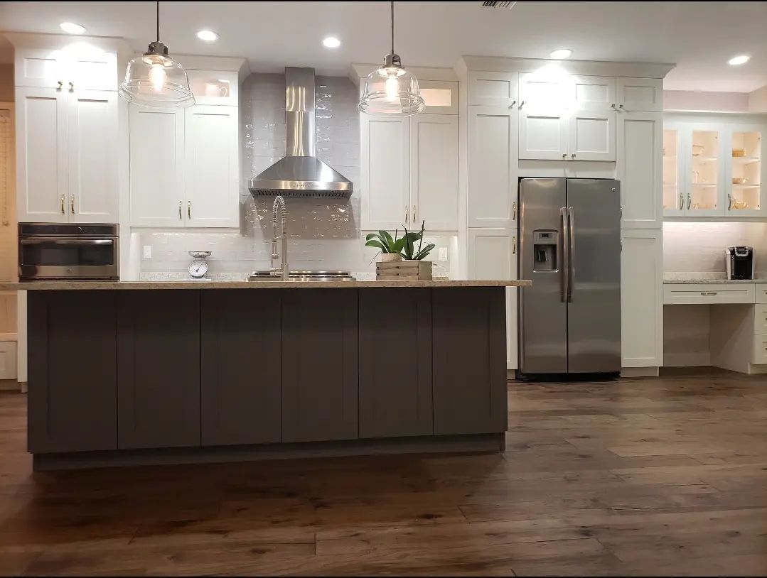 Modern white kitchen with dark island, stainless steel appliances, and hardwood floors