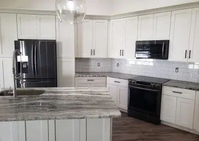 Modern white kitchen with black appliances, marble island, and wood flooring