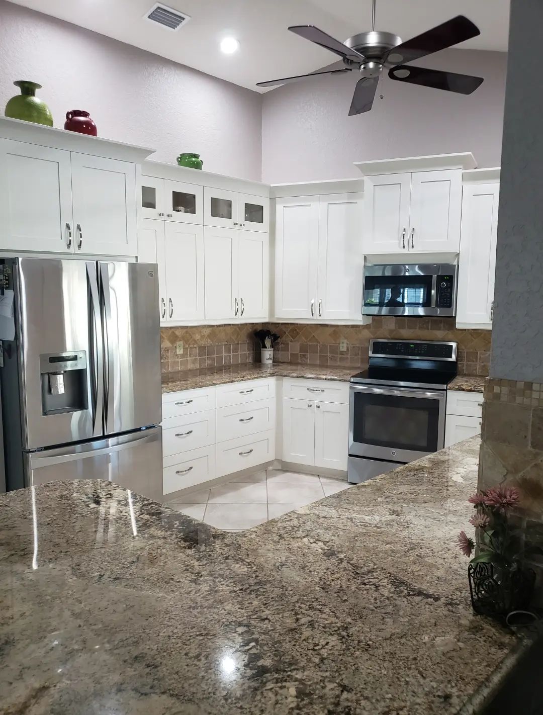 Bright modern kitchen with white cabinets, stainless appliances, granite counters, and ceiling fan.
