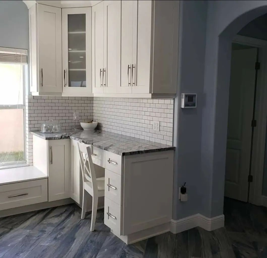 Bright white kitchen with marble counters, tile backsplash, and a small desk nook by a window.