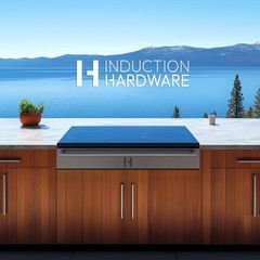 Outdoor kitchen with blue-topped grill by a lake, branded “Induction Hardware,” against a mountain backdrop