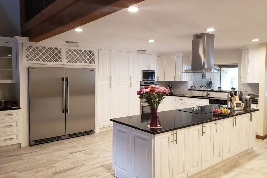 Modern kitchen with stainless steel appliances, black island countertop, white cabinets, and flowers on the island