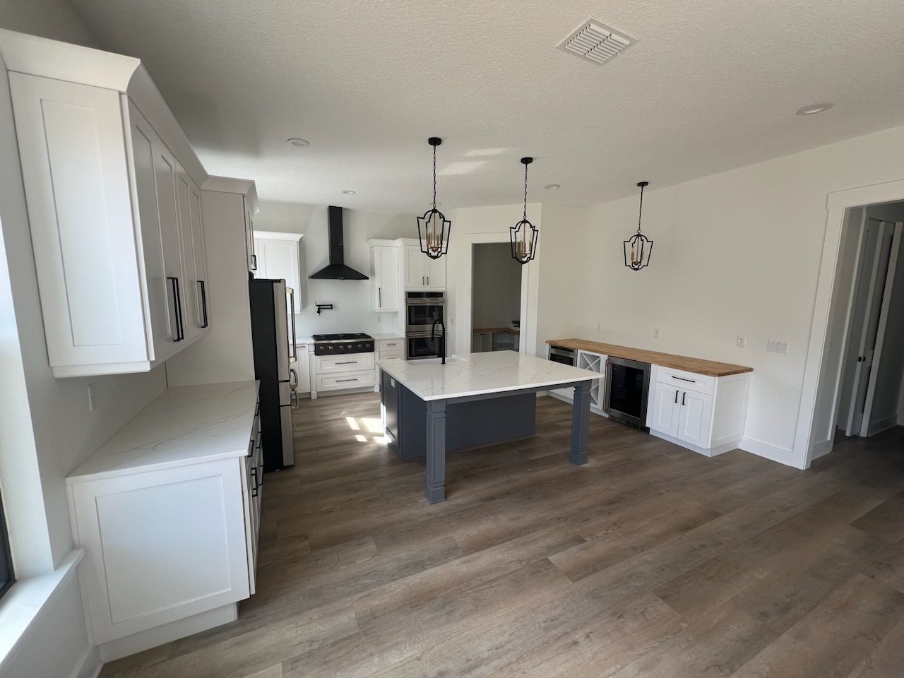 Bright modern kitchen with white cabinets, dark island, wood floors, and pendant lights