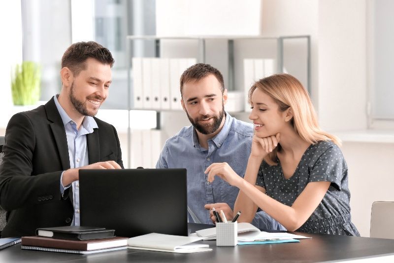 A man and a woman are sitting at a table looking at a laptop.