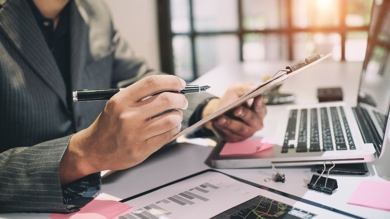A man is sitting at a desk holding a clipboard and a pen.