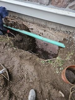 A green pipe is being installed in a hole in the ground