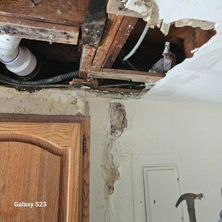 A hole in the ceiling of a kitchen with a hammer