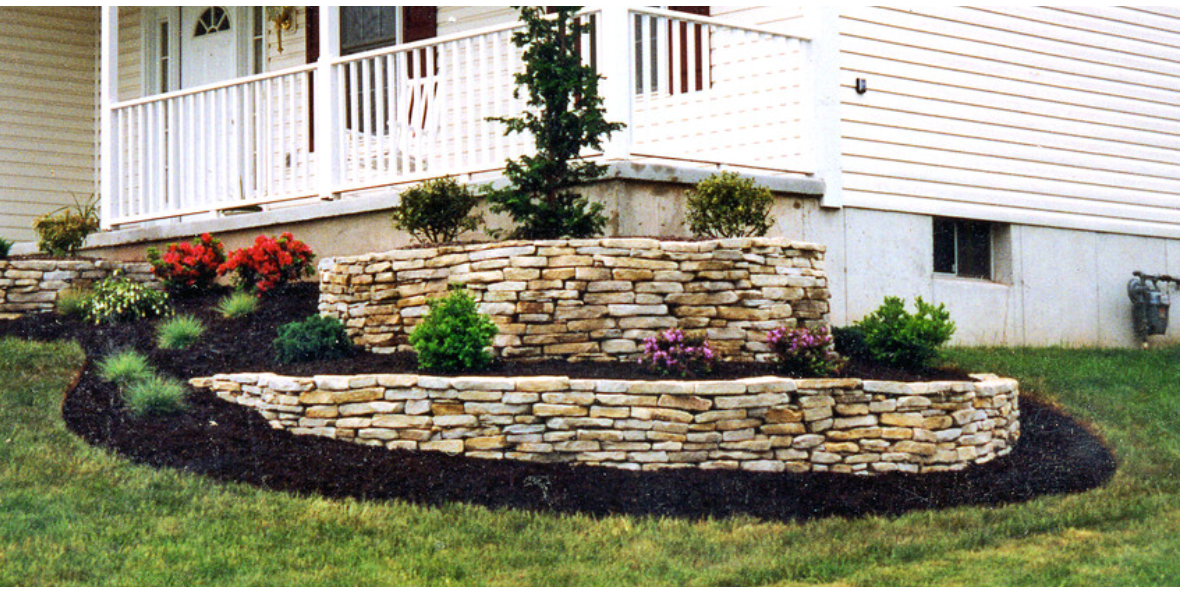A stone wall in front of a house with flowers in it