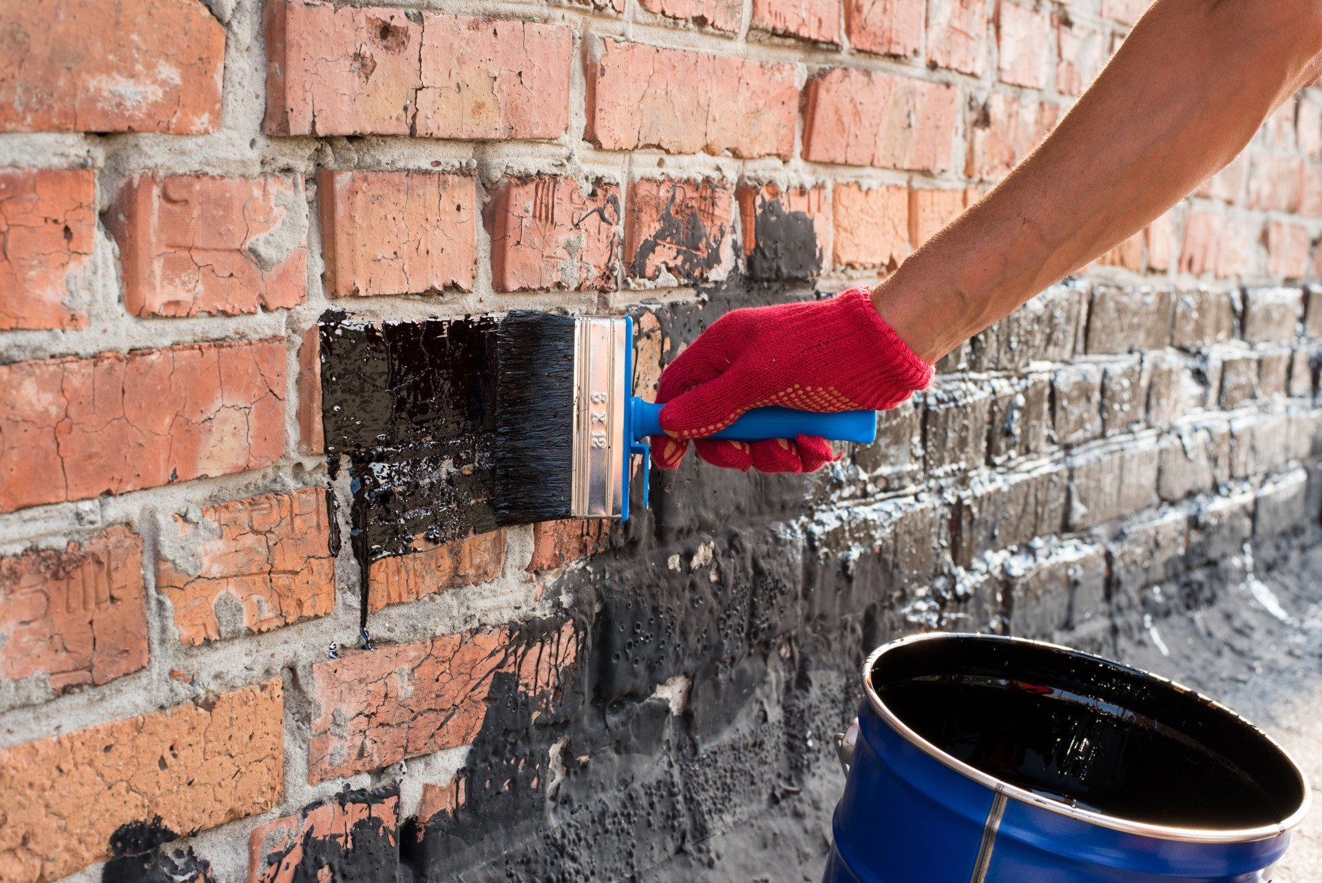 A person is painting a brick wall with a brush.
