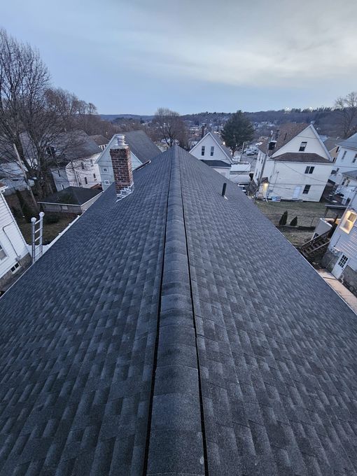 An aerial view of a roof with a chimney and a row of houses in the background.