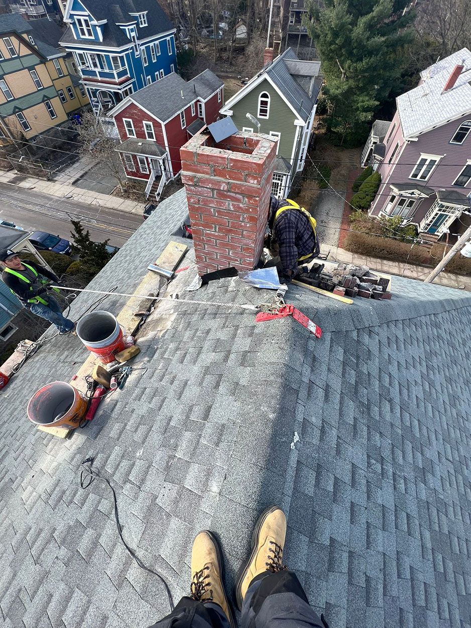 A person is standing on top of a roof next to a chimney