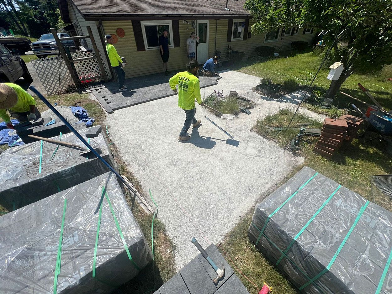 A group of men are working on a concrete driveway in front of a house