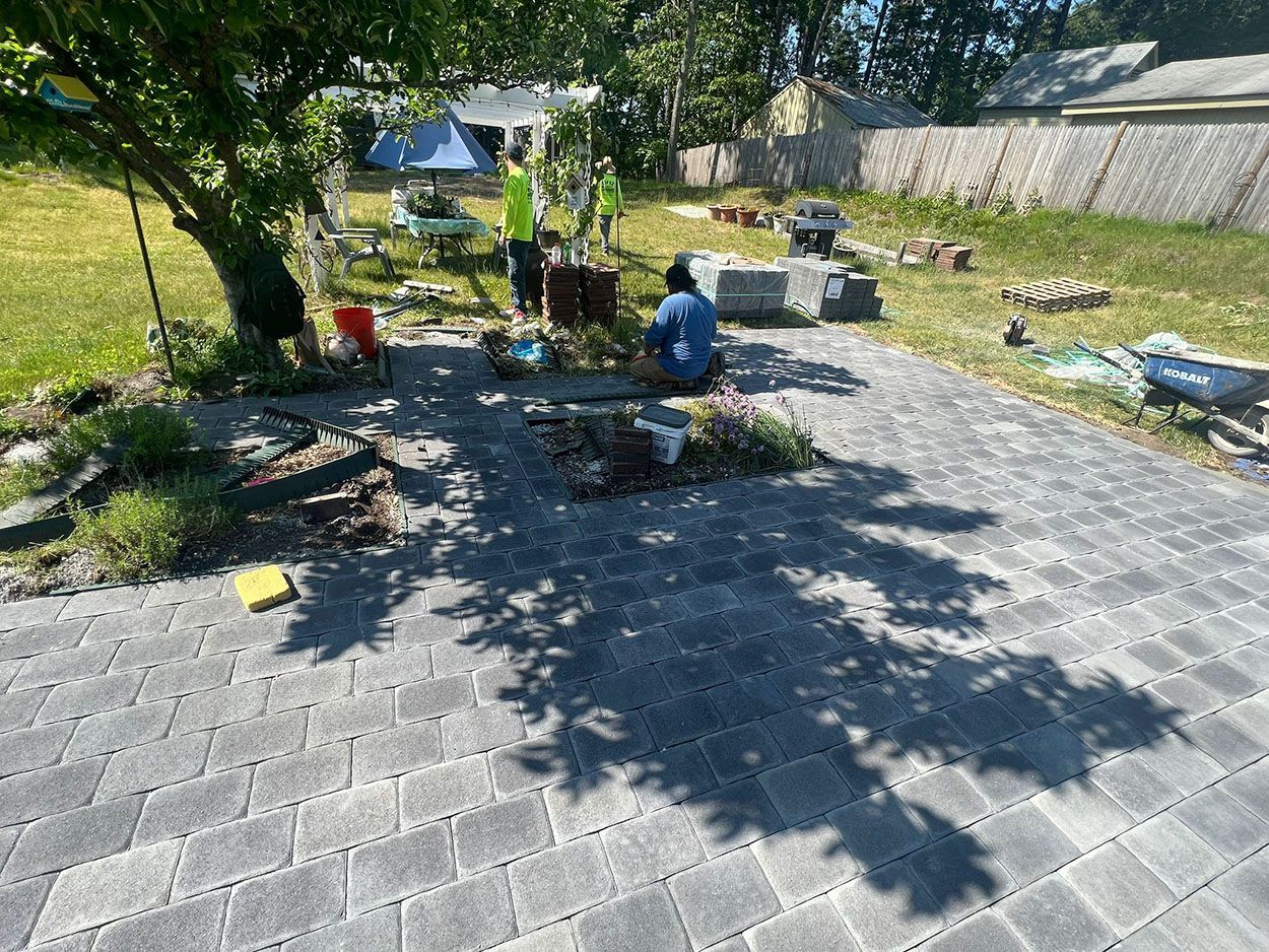 Men working on a brick patio in a backyard