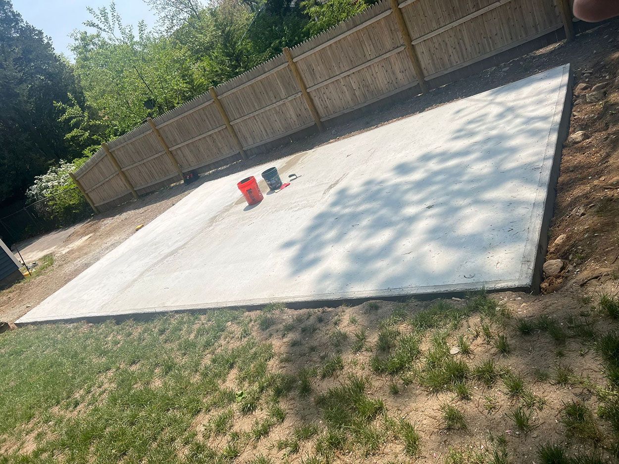 A large concrete slab in a backyard next to a wooden fence