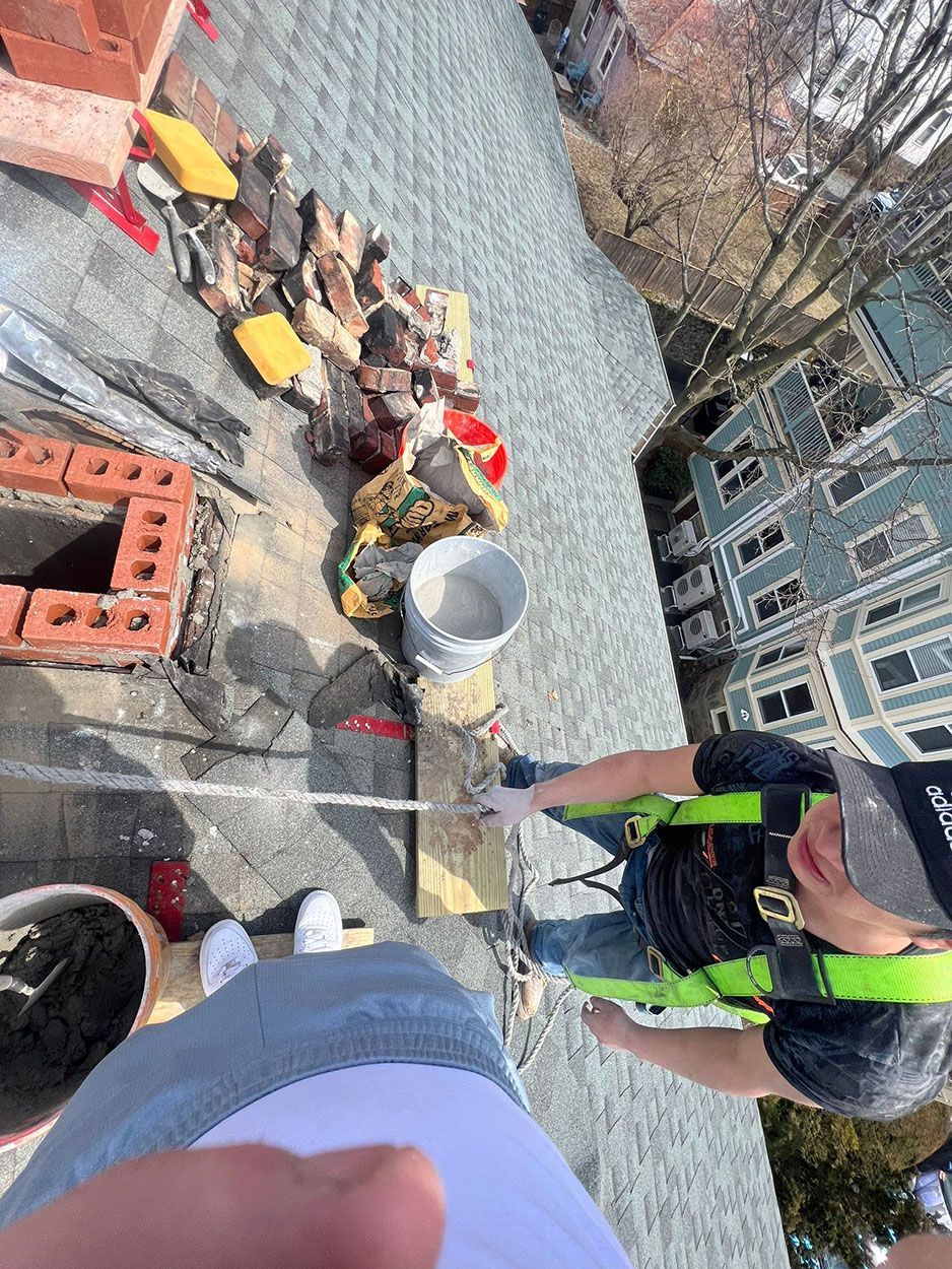 Two men are standing on top of a roof working on a chimney