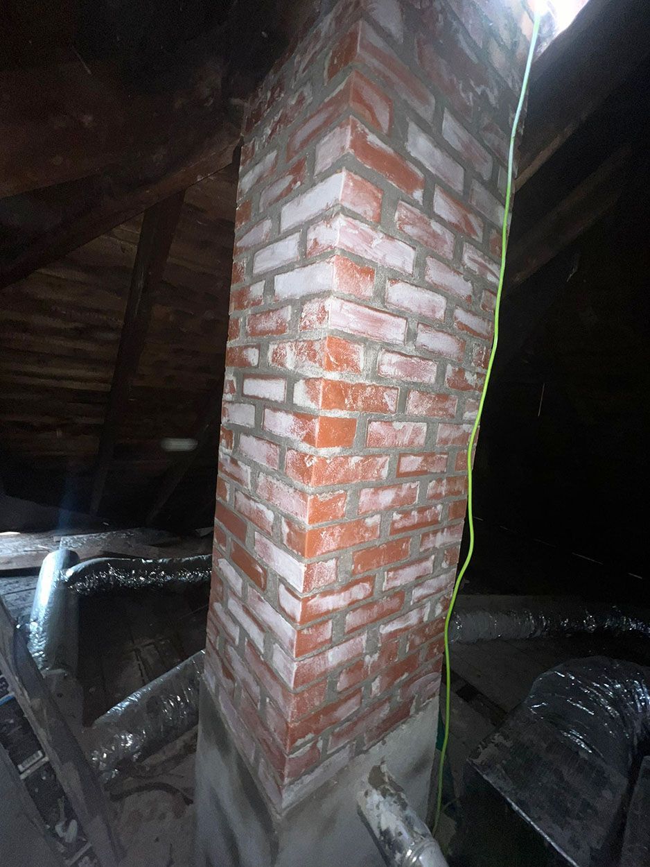 A brick chimney is being built in the attic of a house