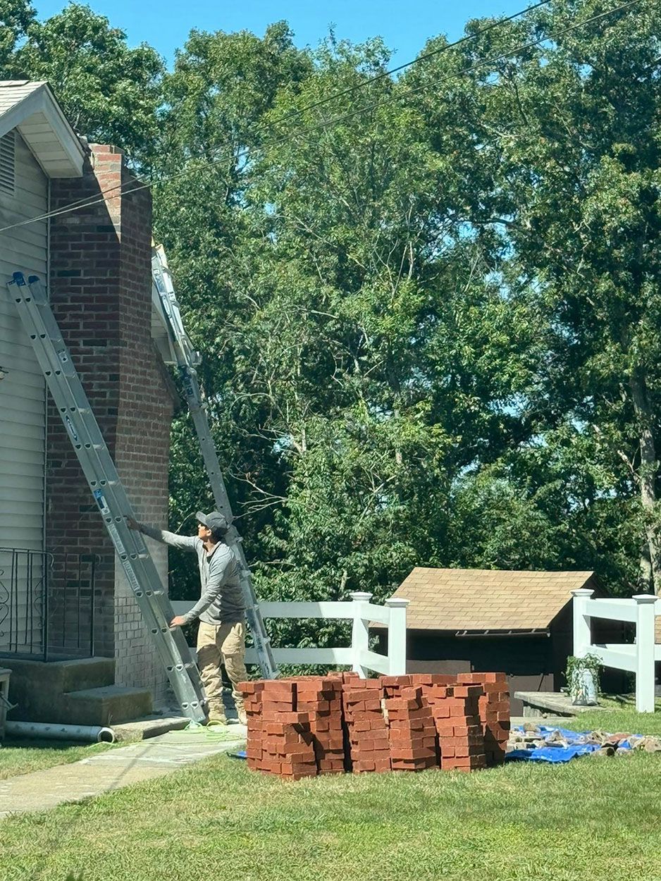 A man is standing on a ladder in front of a brick chimney