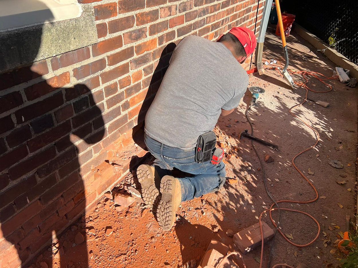 A man is kneeling removing the old brick wall