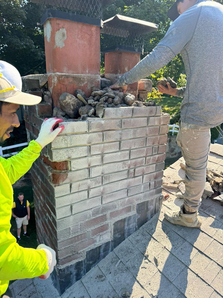 Two men are working on a brick chimney on a roof
