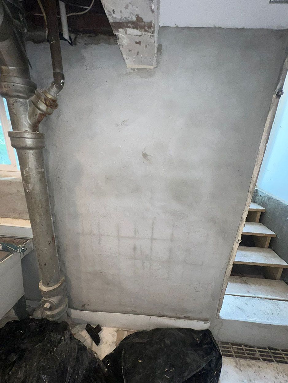 A staircase in a basement with a concrete wall and pipes