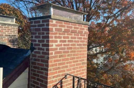 A brick chimney is sitting on top of a roof next to a tree.