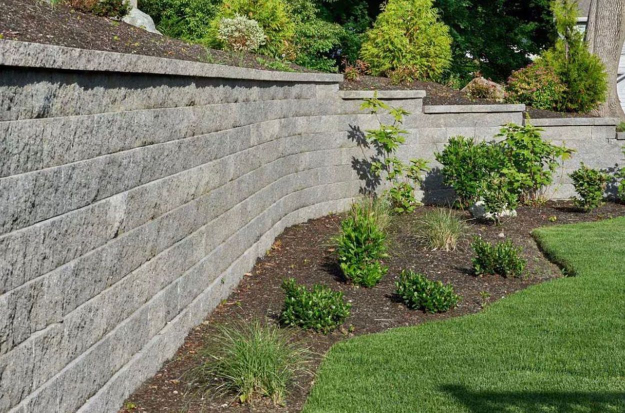 A stone wall surrounds a lush green lawn in a backyard