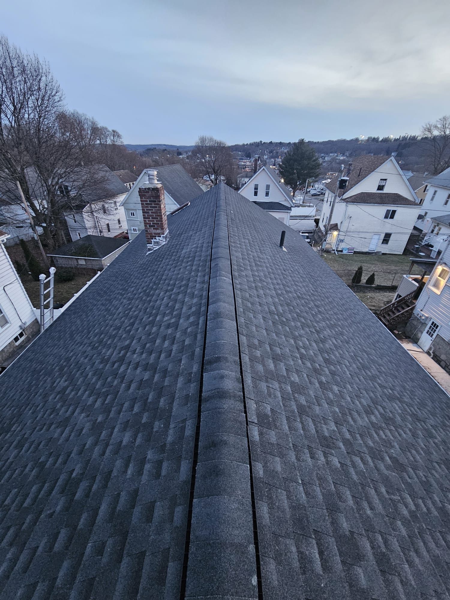 A roof with a chimney on it is surrounded by houses in a small town.