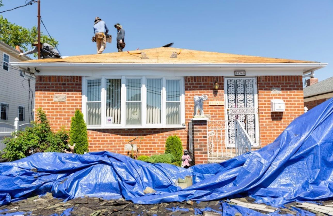 Two men are working on the roof of a brick house.