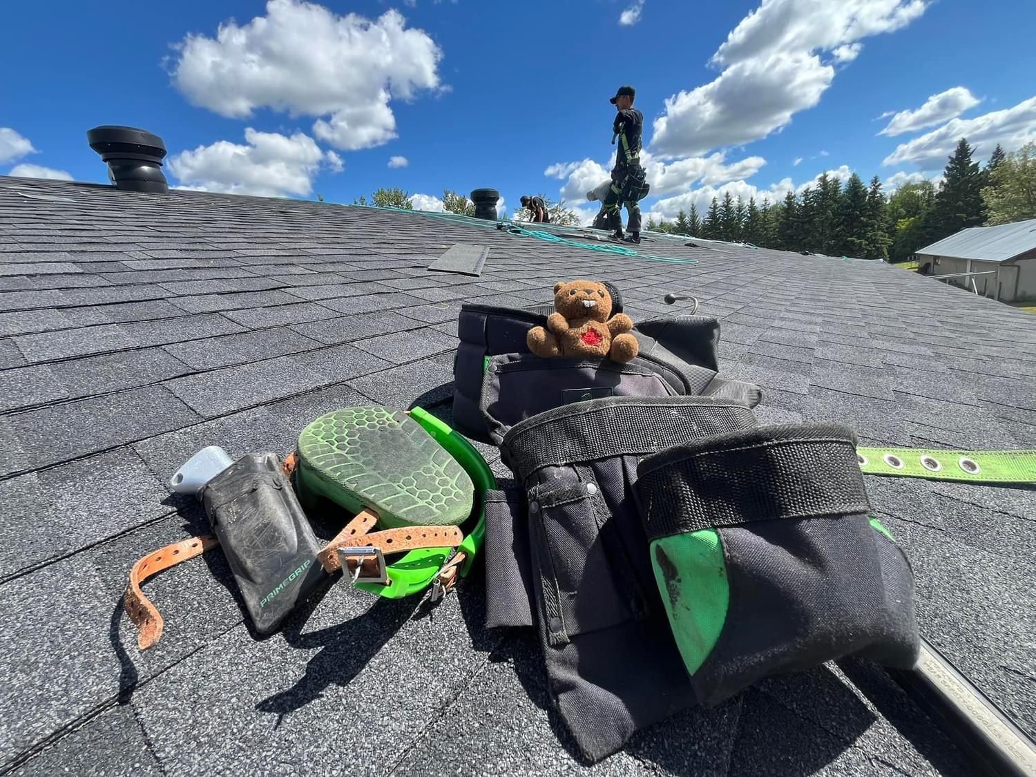 A teddy bear is sitting on top of a tool bag on a roof.