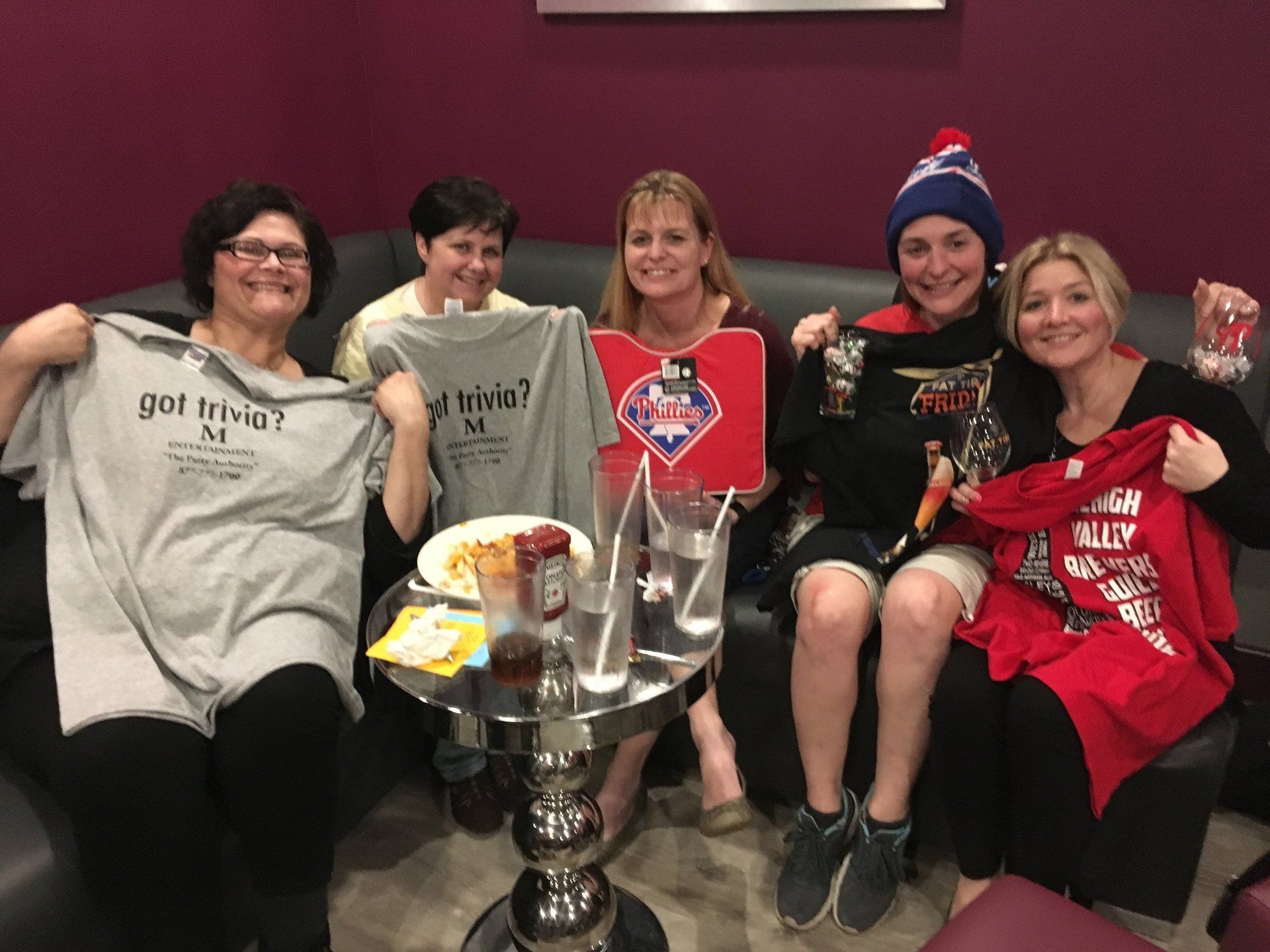 A group of women are sitting on a couch holding up t-shirts.