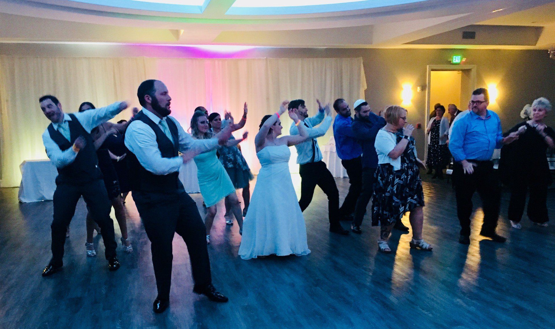 A group of people are dancing in a room at a wedding reception.