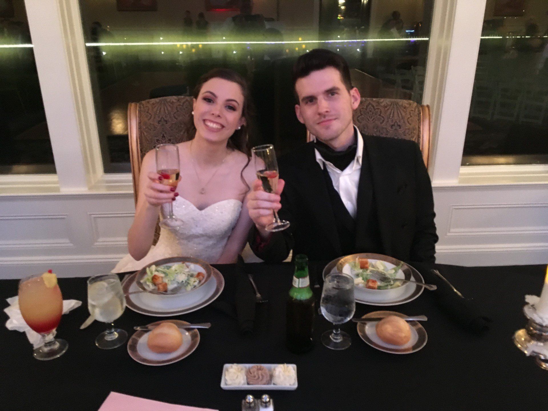 A bride and groom are sitting at a table holding champagne glasses