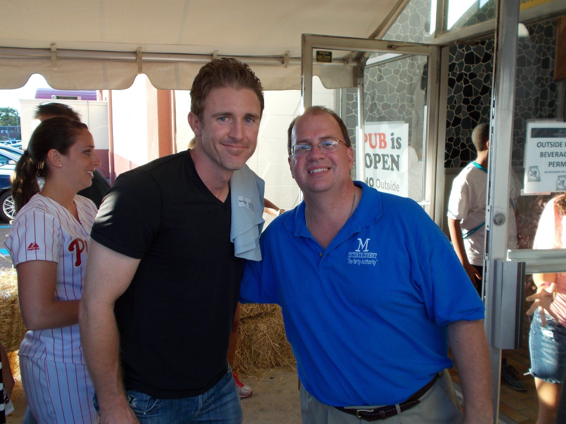 Two men pose for a picture in front of a sign that says pub is open