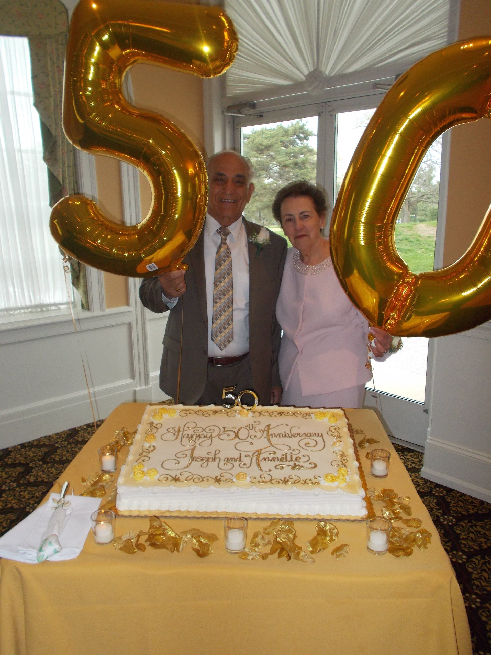 A man and woman standing next to a 50th anniversary cake