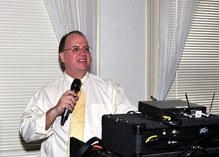 A man in a white shirt and yellow tie is holding a microphone.