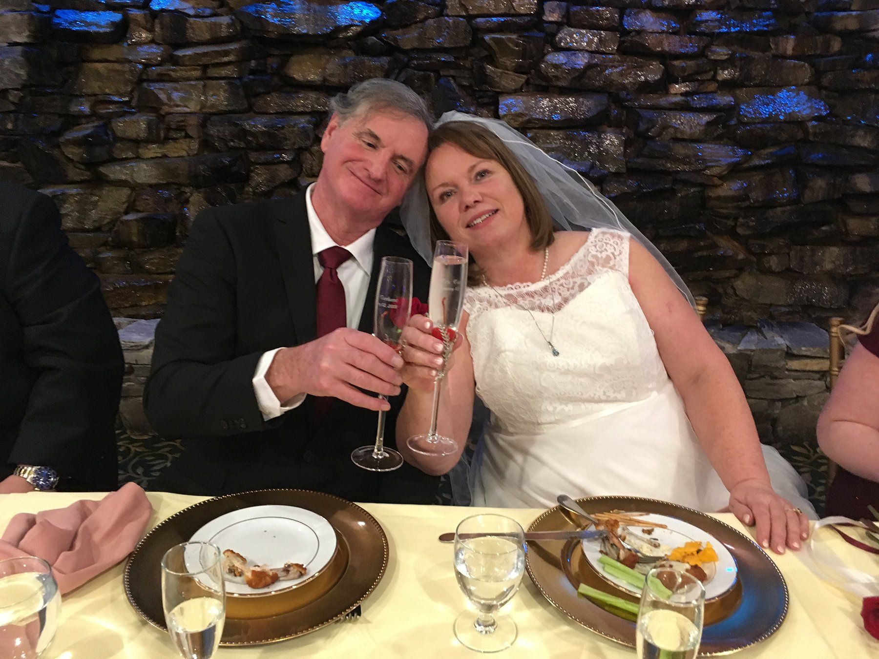 A bride and groom are sitting at a table holding champagne glasses.