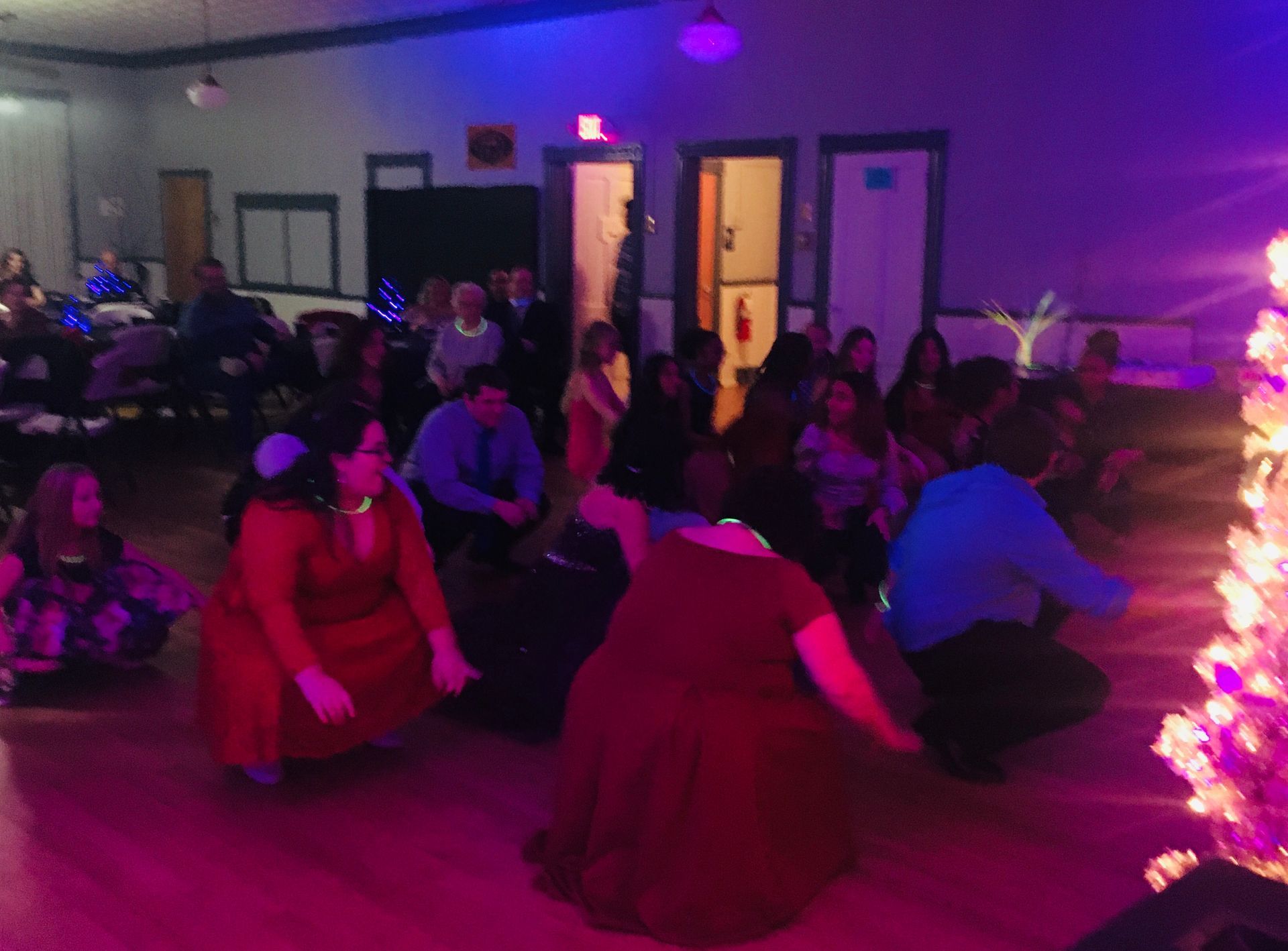 A group of people are dancing in a room with a christmas tree in the background.