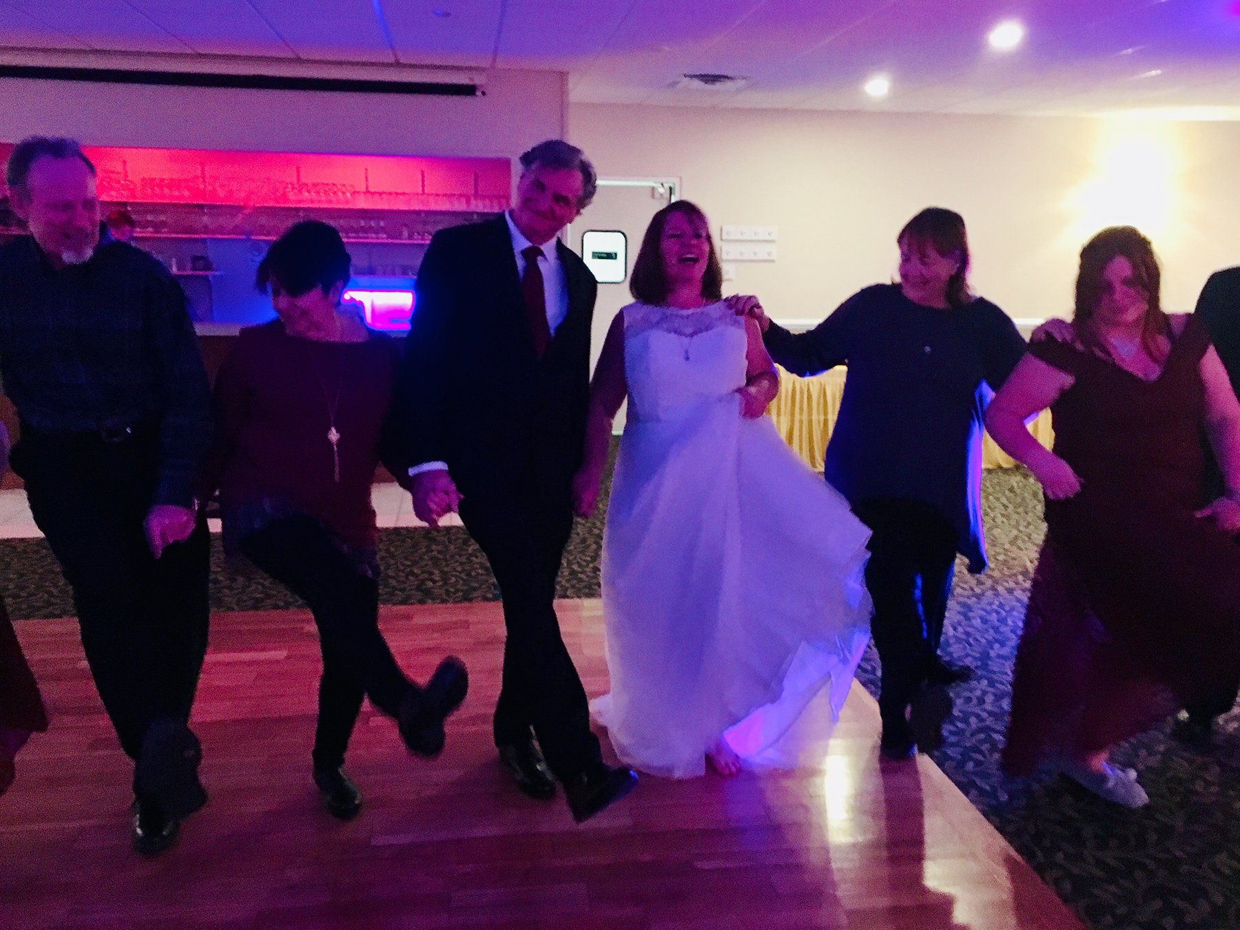 A bride and groom are dancing with their family at a wedding reception.