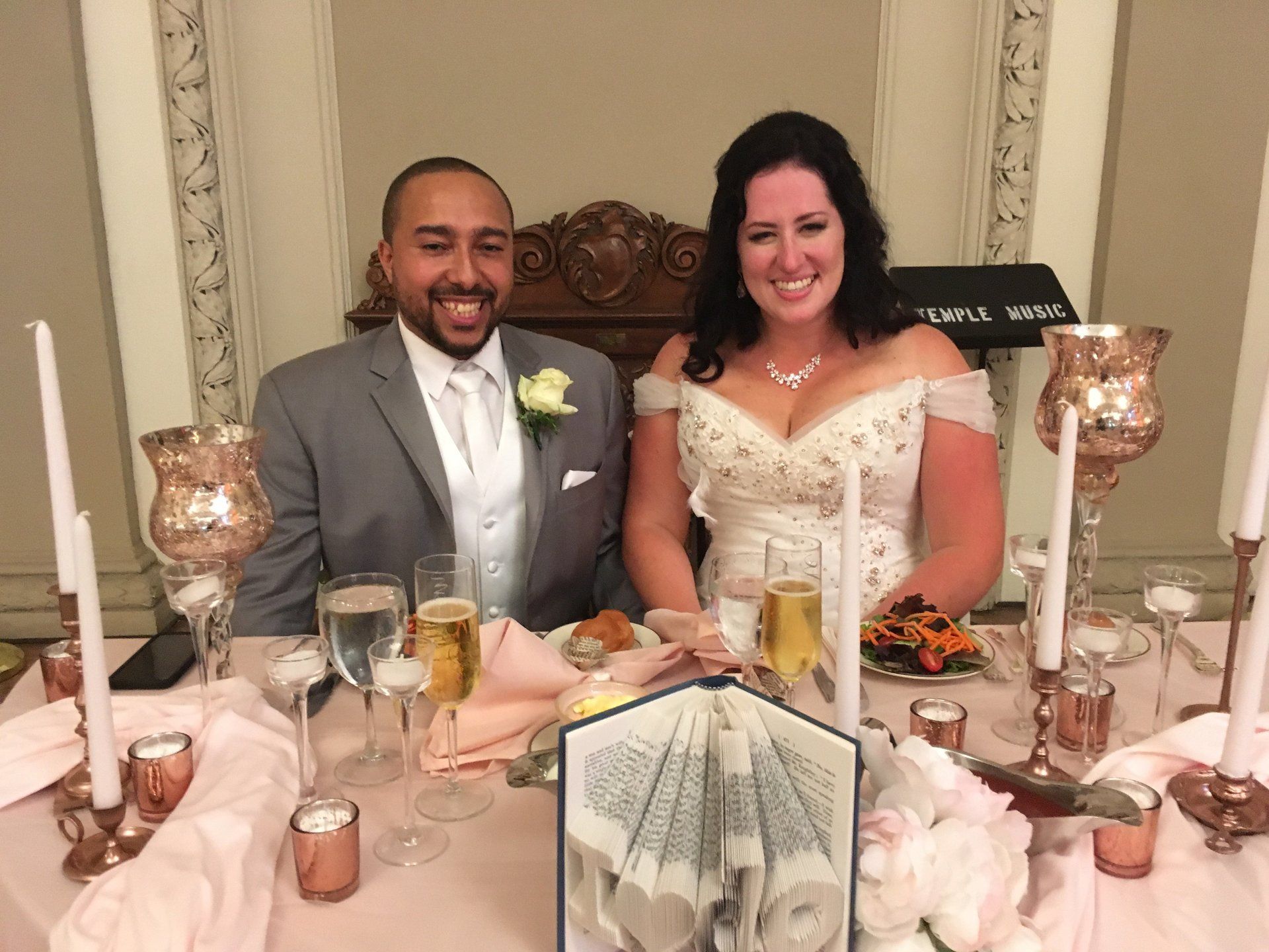 A bride and groom are sitting at a table with wine glasses and candles.