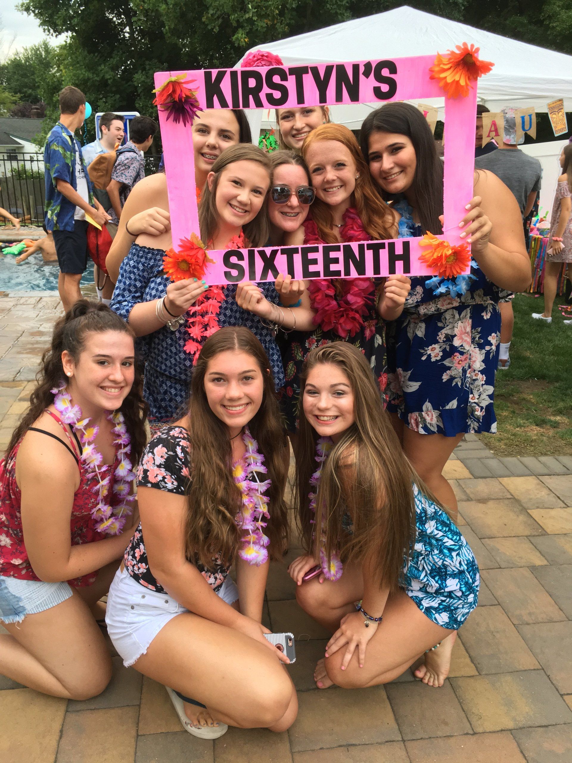 A group of girls are posing for a picture with a sign that says kirsty 's sixteenth