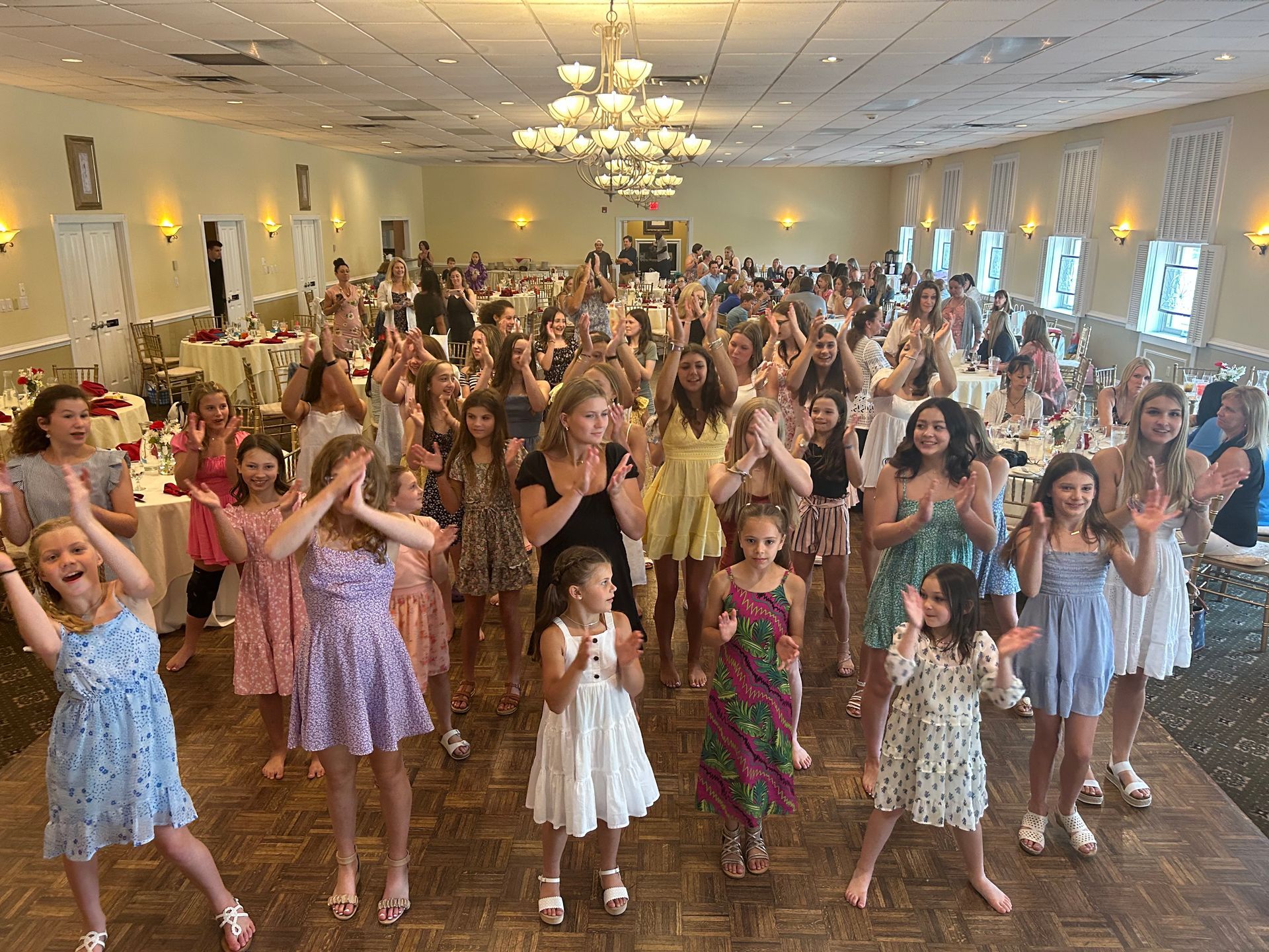 A large group of young girls are dancing in a large room.
