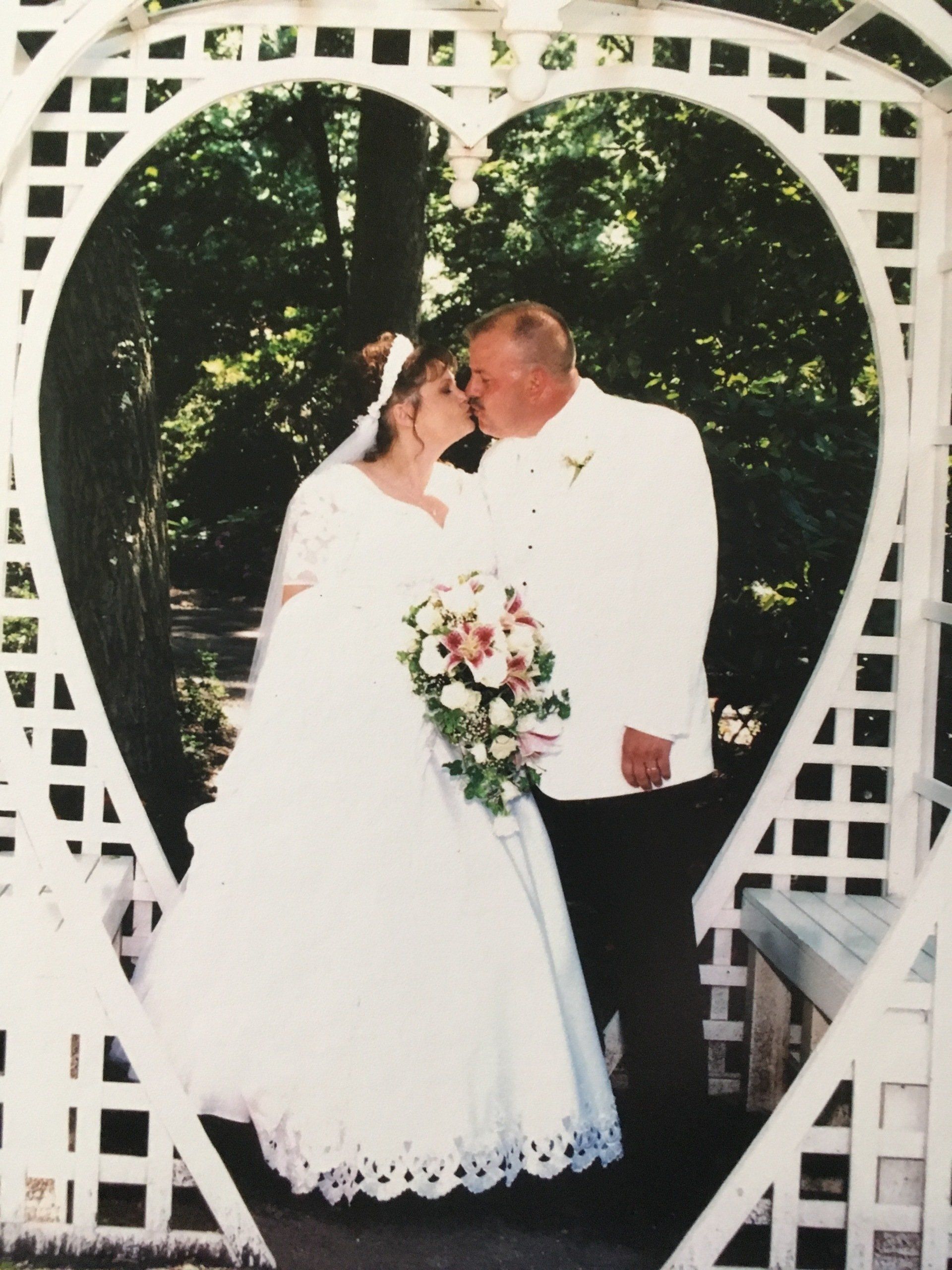 A bride and groom kiss under a heart shaped archway