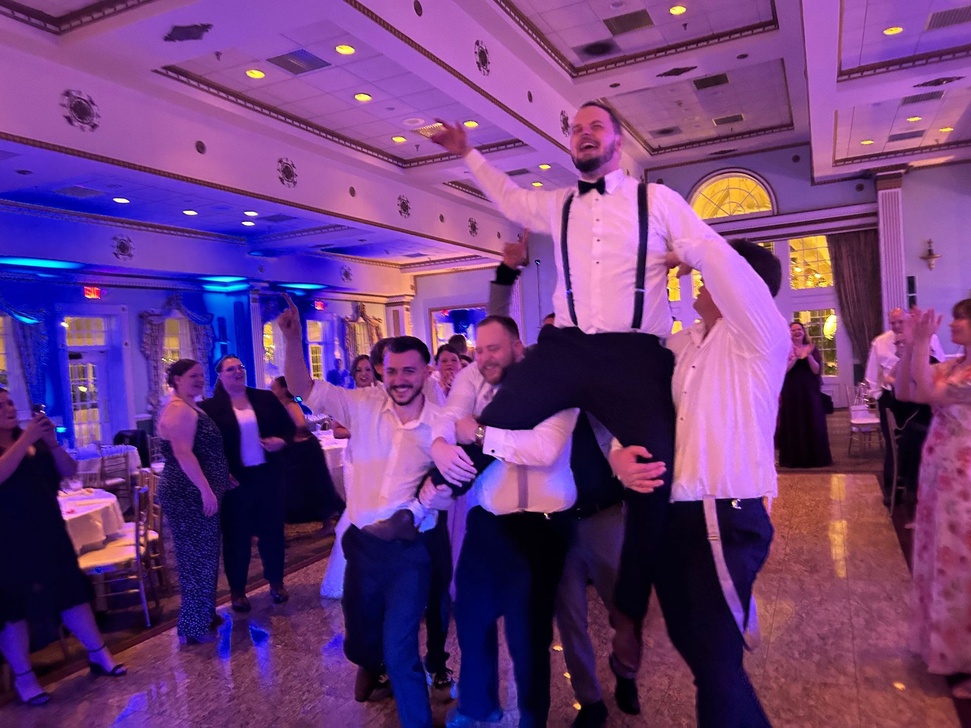 A group of men are carrying a man in their arms at a wedding reception.